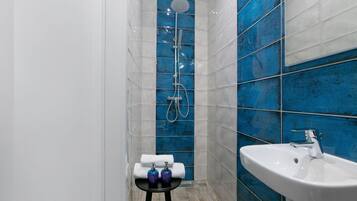 Een badkamer met een witte wastafel, een douchegedeelte betegeld met blauwe tegels, en een klein krukje met toiletartikelen.