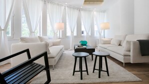 Una sala de estar moderna con un sofá blanco, dos taburetes negros, una mesa de centro y un banco.