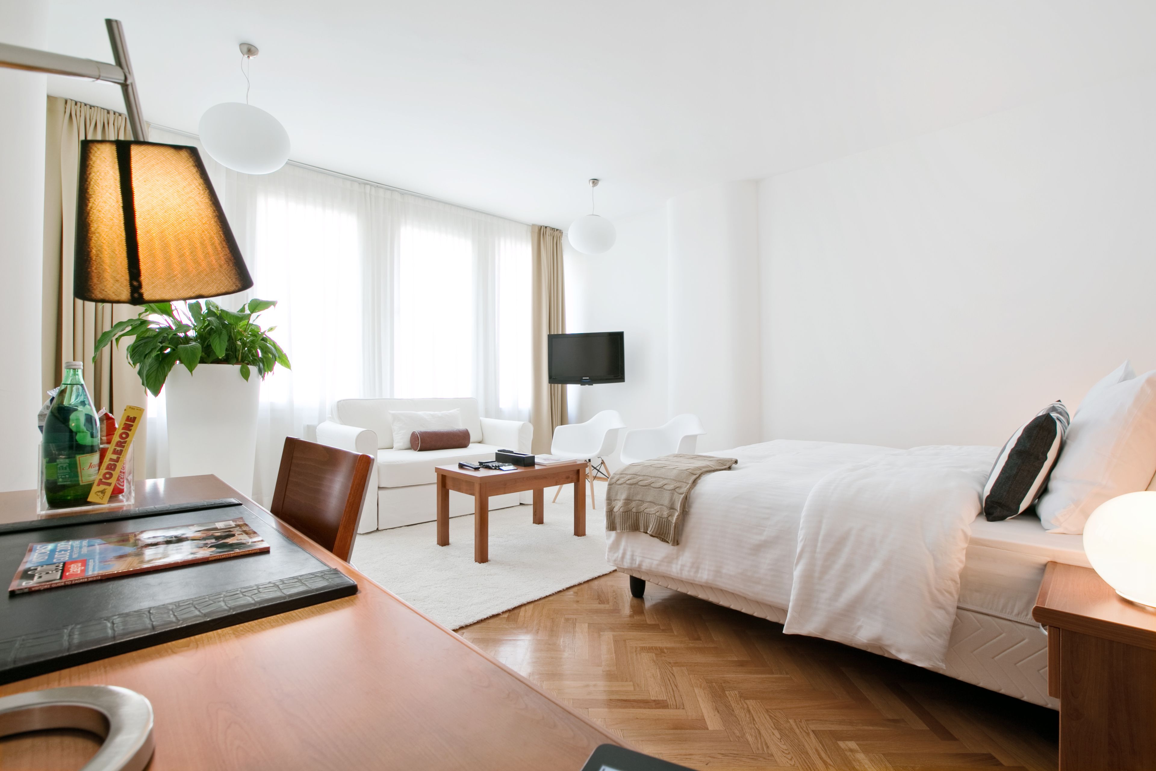 Una habitación de hotel con una cama, un escritorio con lámpara, un televisor y una planta.