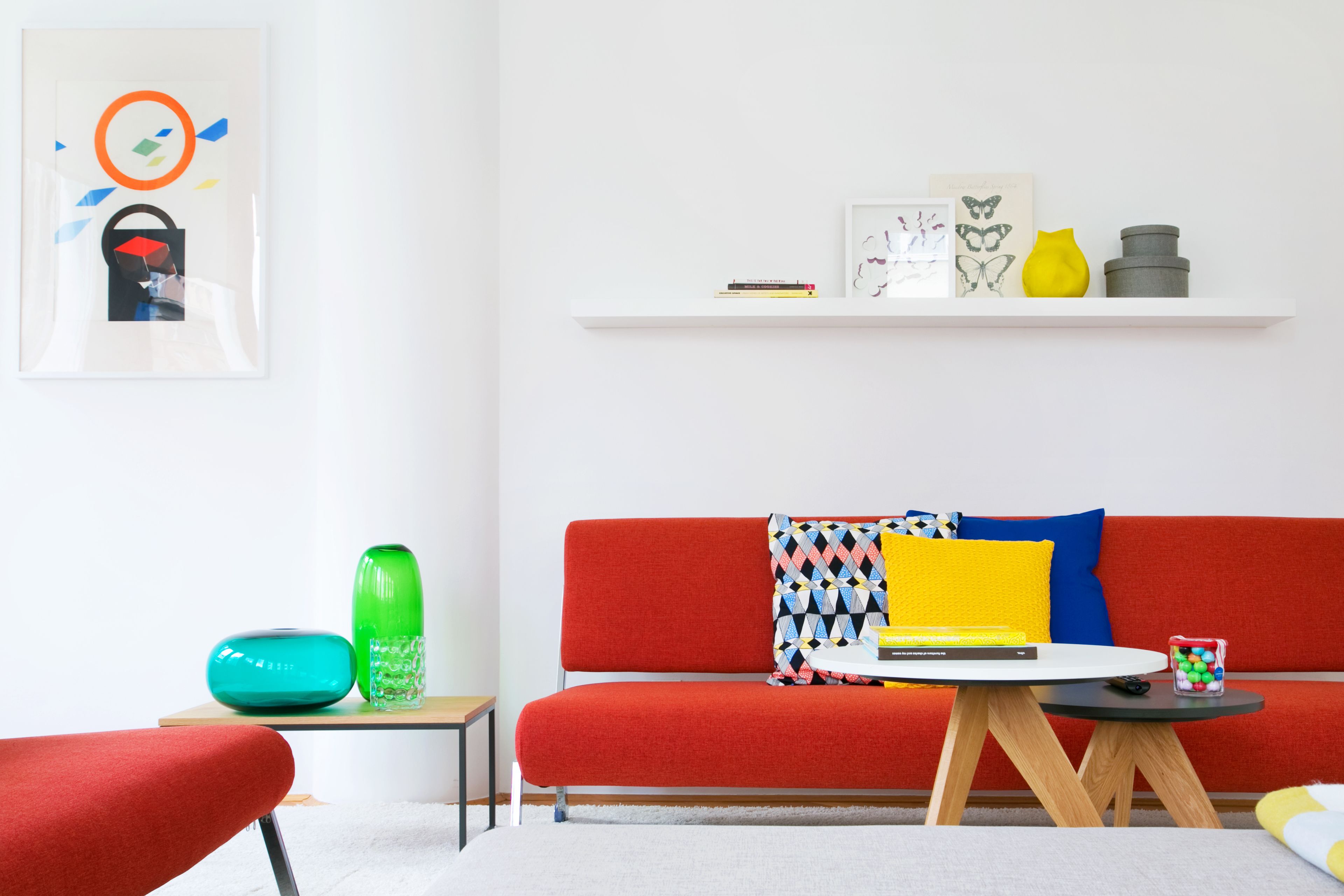A modern living room with a red sofa, a small table with a laptop, and a colorful vase.