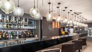 A bar area with a long counter, multiple hanging light fixtures, and bar stools.