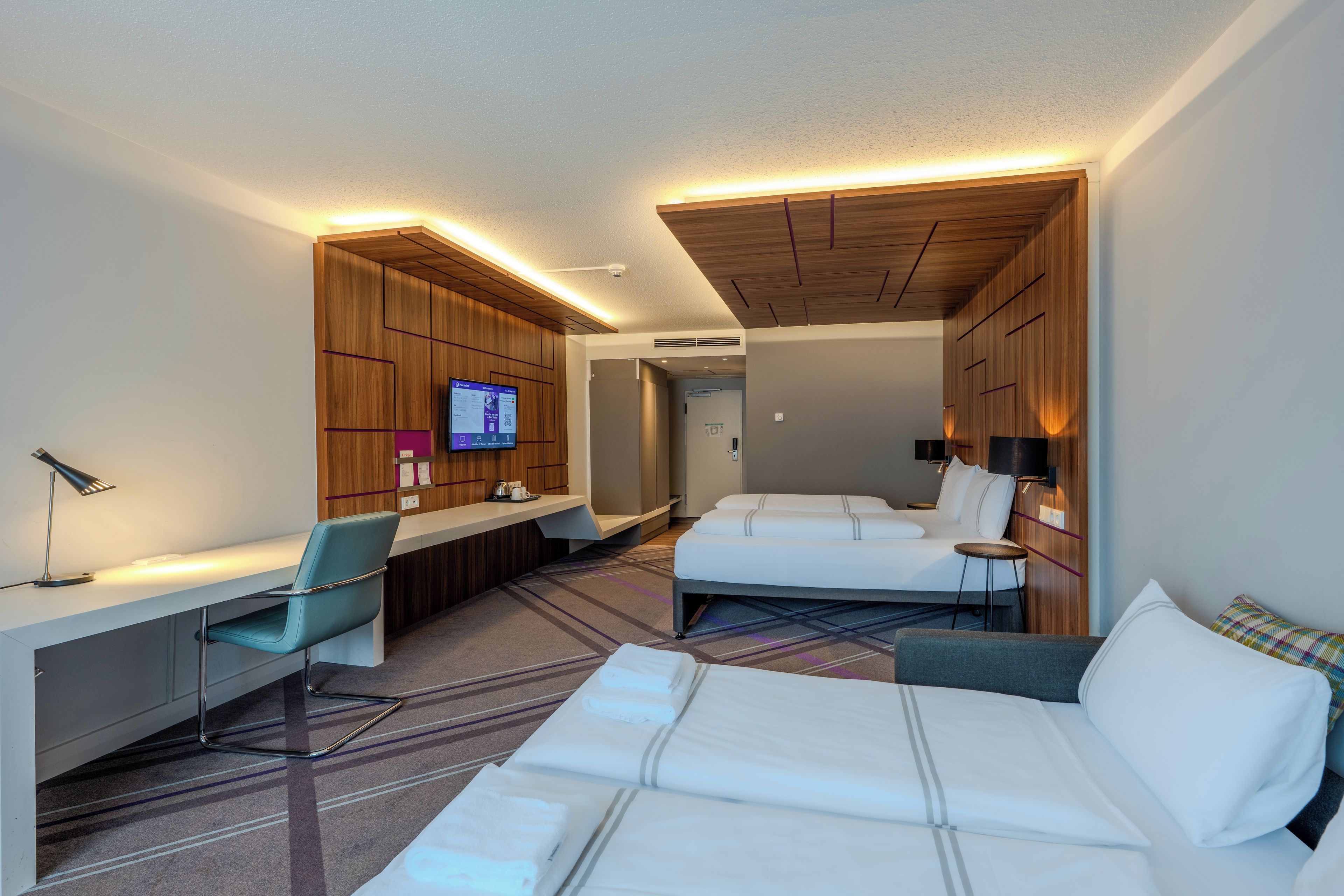 A hotel room with a bed, a desk, a chair, a TV, and a bathroom.