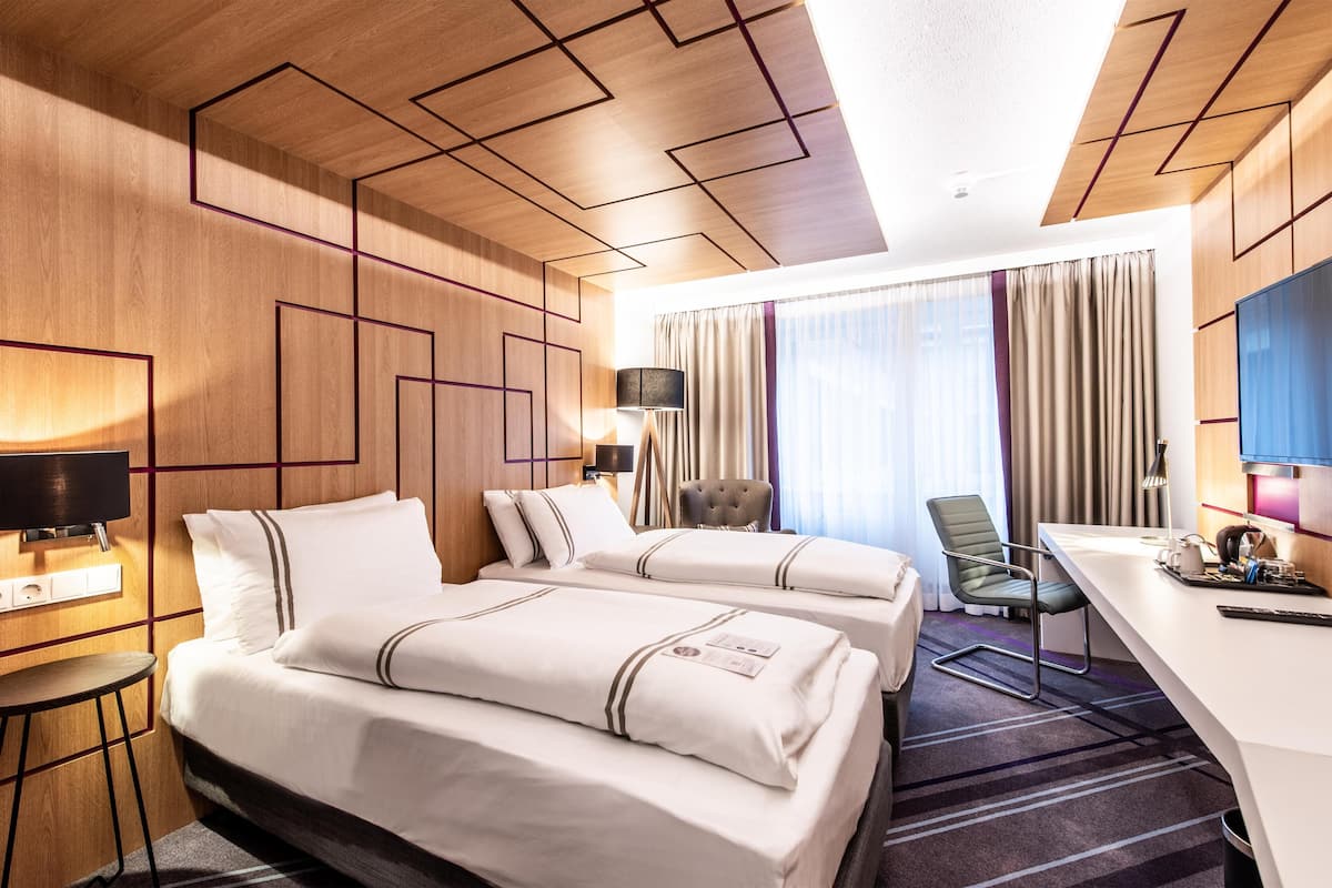 A hotel room with two beds, a desk, a chair, a TV, and a window with curtains.
