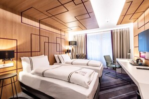 A hotel room with two beds, a desk, a chair, a TV, and a window with curtains.