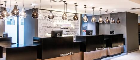 A hotel reception area with black reception desks, hanging light fixtures, and a wall with motivational phrases.