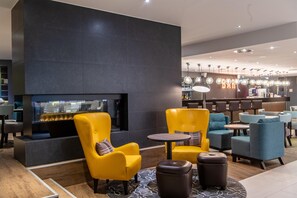 A modern lounge area with a fireplace, yellow and blue seating, and a bar in the background.