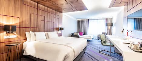 Una habitación de hotel moderna con una cama grande, un escritorio, una silla y un ventanal con cortinas.