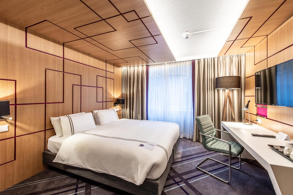A hotel room with a bed, desk, chair, and a large mirror.