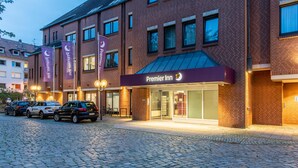A brick building with a marquee sign for Premier Inn, a paved driveway, and parked cars.