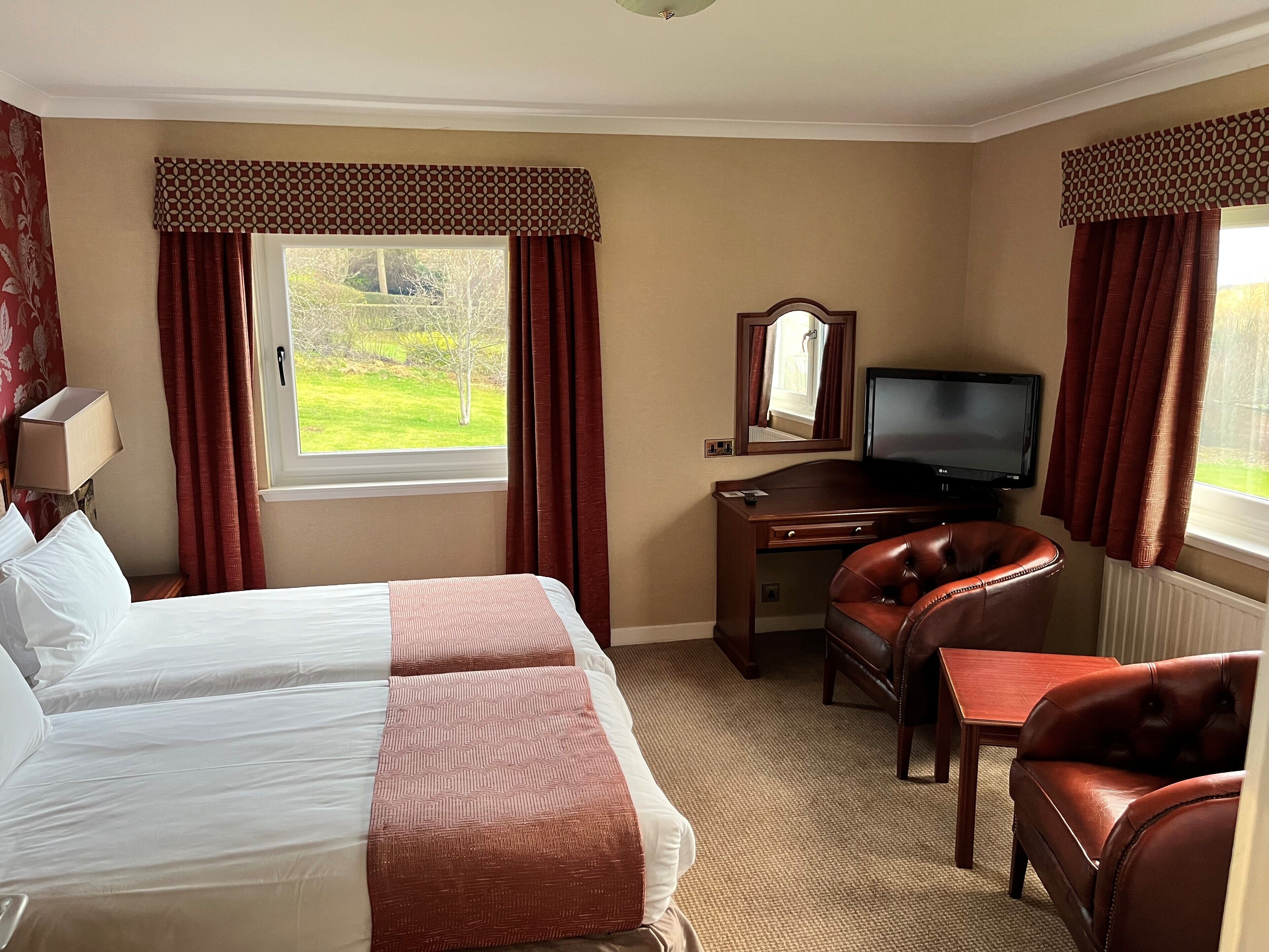 Habitación de hotel con cama, escritorio, silla, televisor y ventana con cortinas.