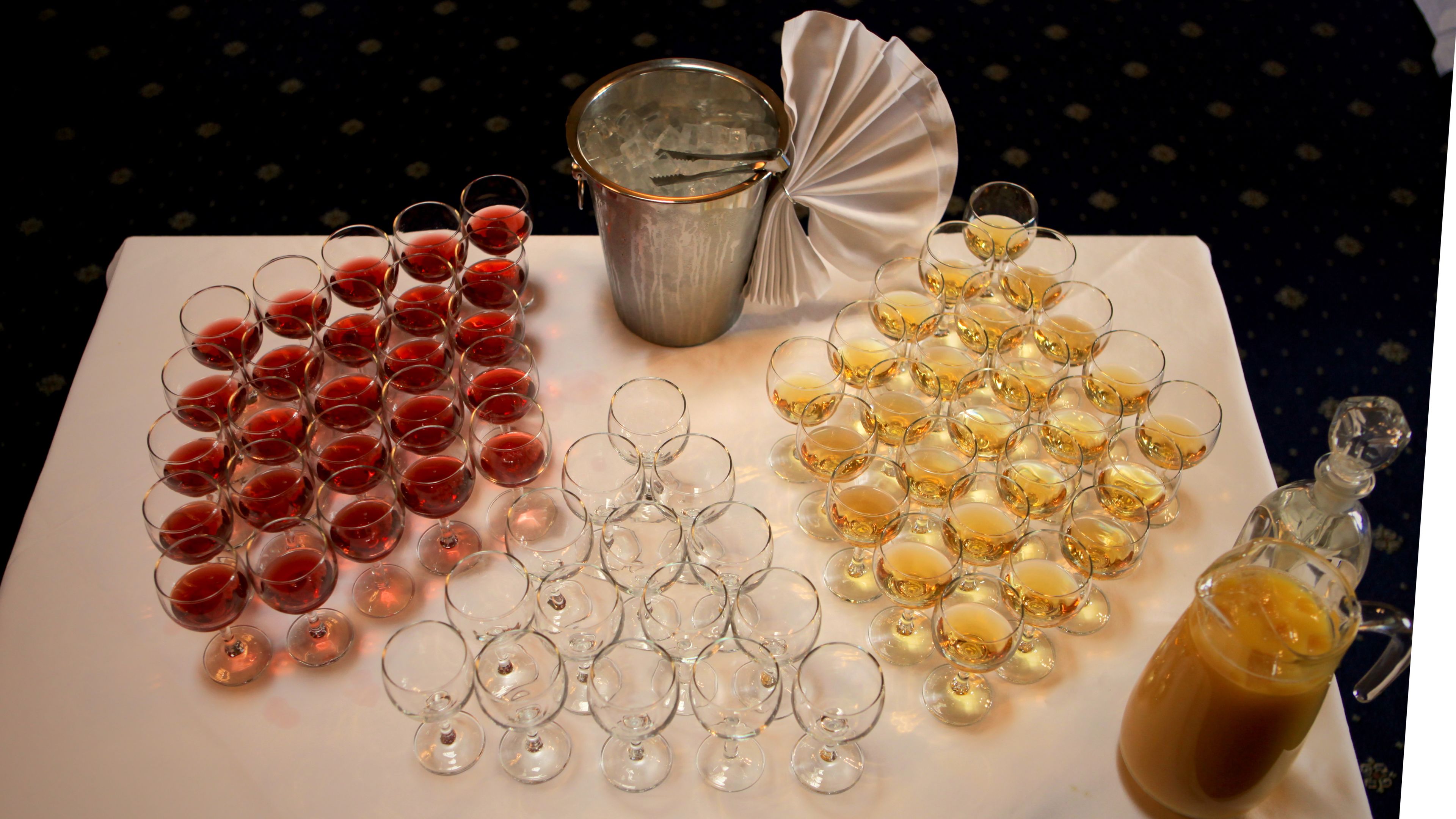 Une table avec plusieurs verres à vin remplis de vin rouge et de vin blanc, un pichet en métal et une bouteille de whisky.