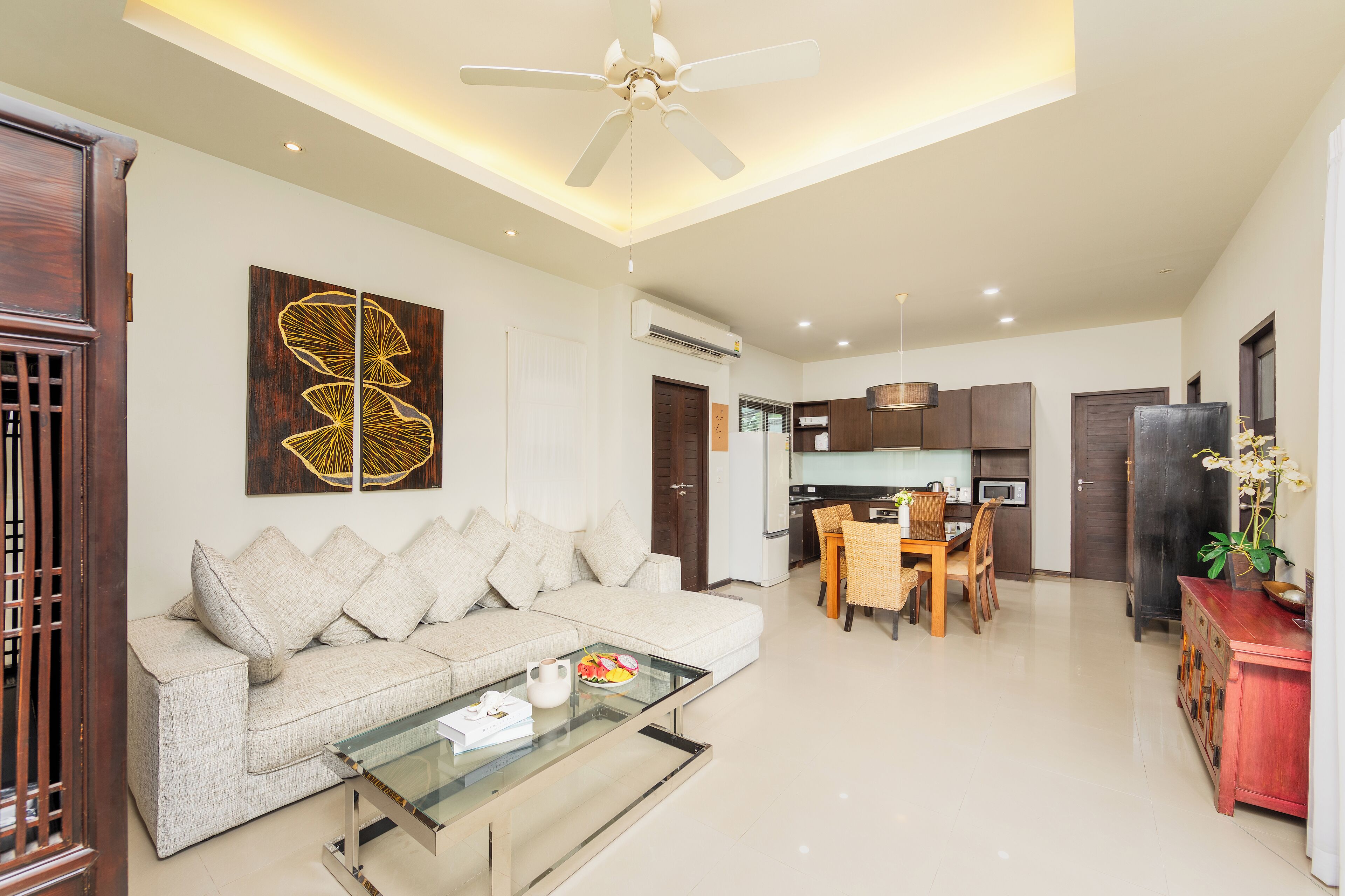 A modern living room with a sofa, glass coffee table, and a dining area with chairs and a table.