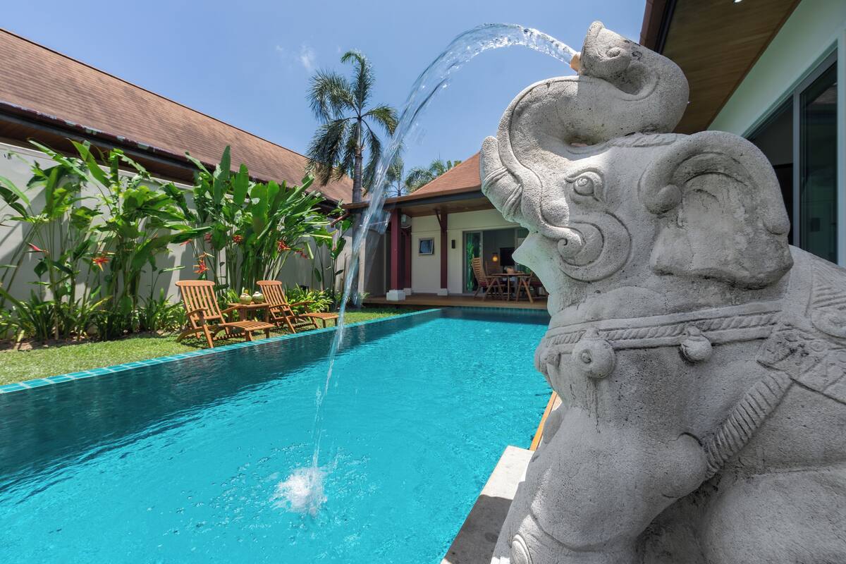 Ein Pool mit einer Springbrunnen, umgeben von tropischen Pflanzen und Holzliegen.