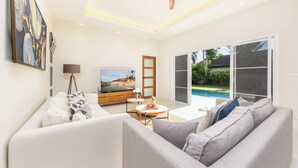 A modern living room with a sofa, a coffee table, a TV, and a view of a swimming pool.