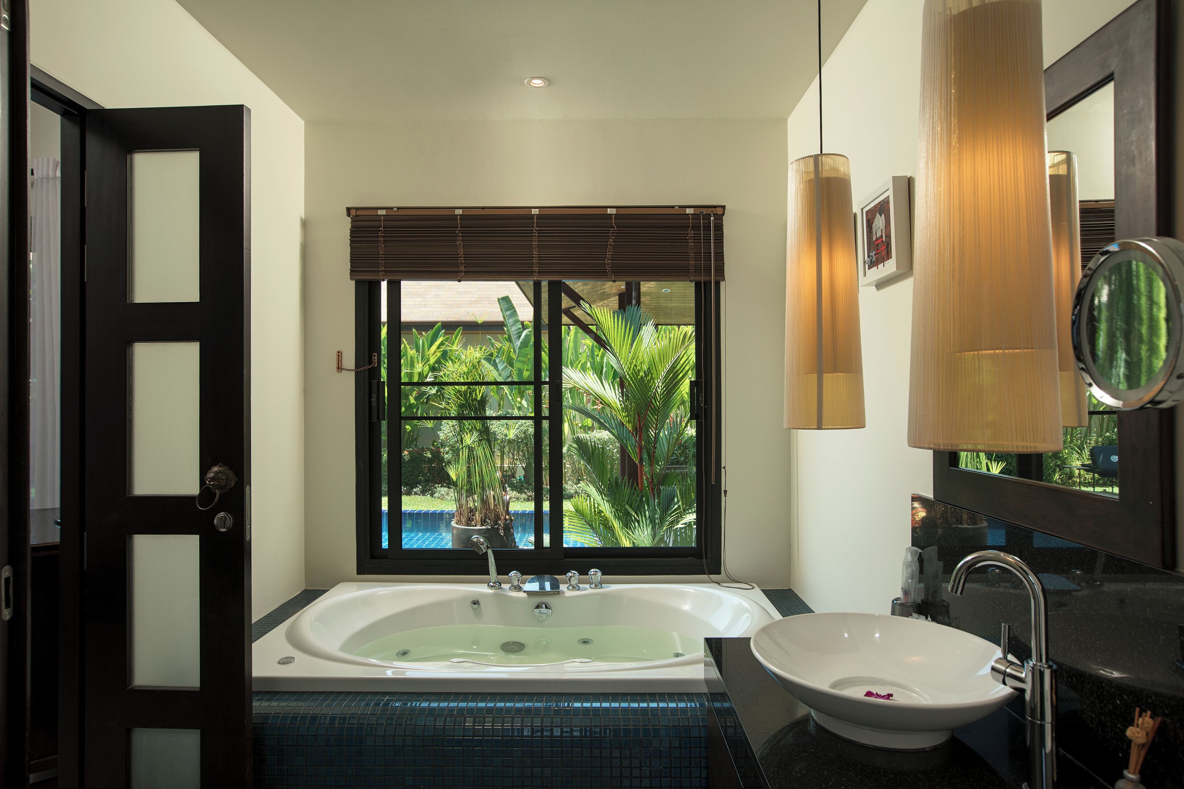A modern bathroom with a bathtub, sink, and large window with blinds.