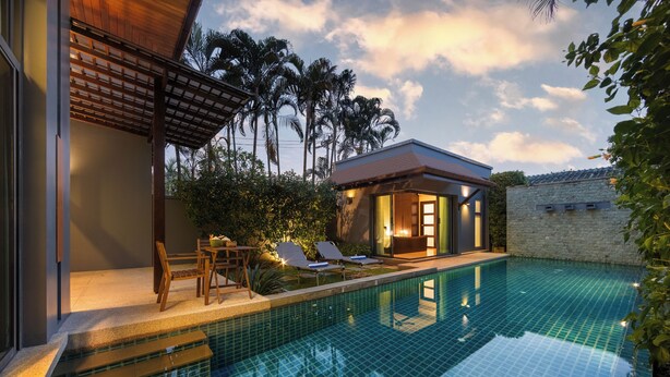 A swimming pool with a tiled deck, lounge chairs, and a small building with a roof.