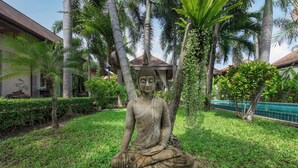 A large Buddha statue in a garden with palm trees and a building in the background.