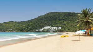 Ein Strand mit klarem türkisblauem Wasser, einem sandigen Ufer und einem Hintergrund aus üppigen, grünen Hügeln.