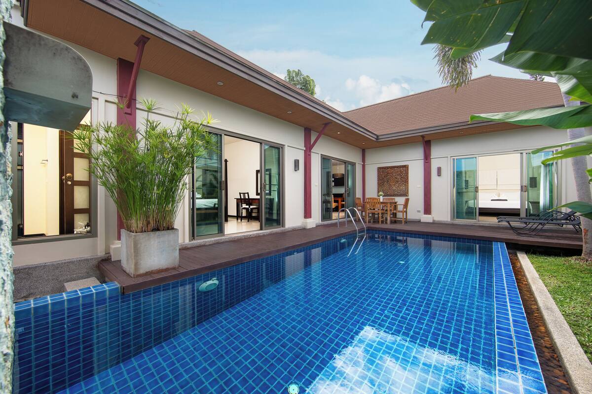 Ein Swimmingpool mit blauen Fliesen, ein Blumentopf und eine Glastür zu einem Raum mit einem Bett.