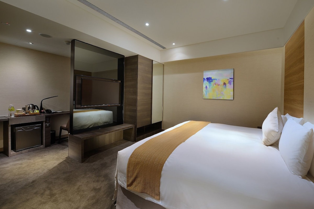 Ein Hotelzimmer mit Bett, Schreibtisch mit Stuhl, Spiegel und einem Gemälde an der Wand.