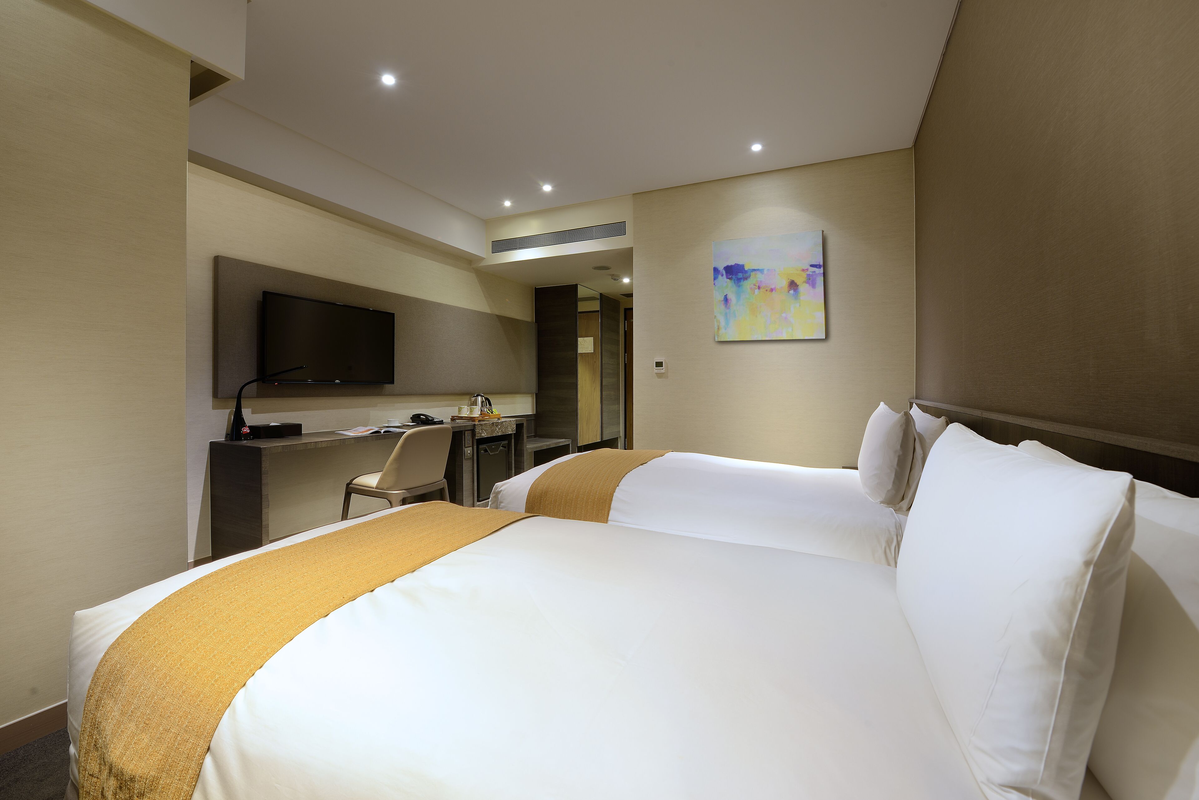 A hotel room with a large bed, a desk, a chair, a television mounted on the wall, and a painting.