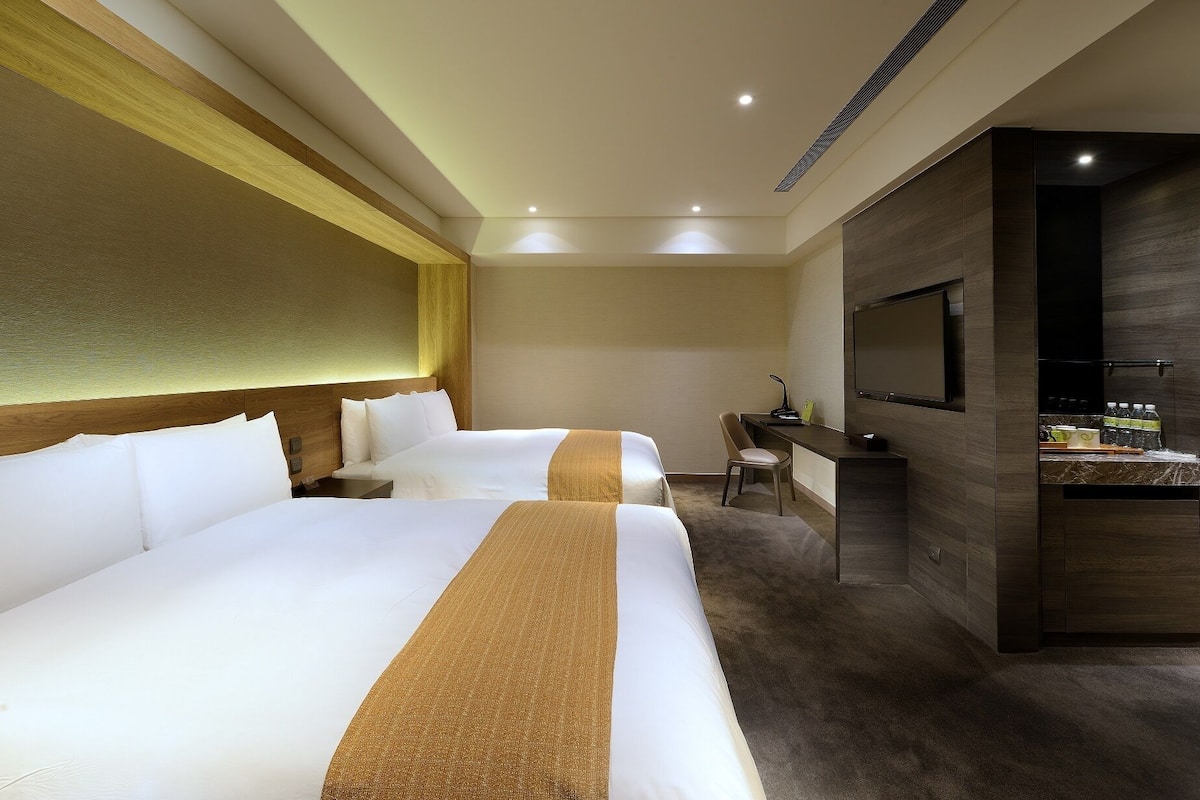 Ein Hotelzimmer mit zwei Betten, einem Schreibtisch, einem Stuhl, einem Fernseher und einer Minibar.