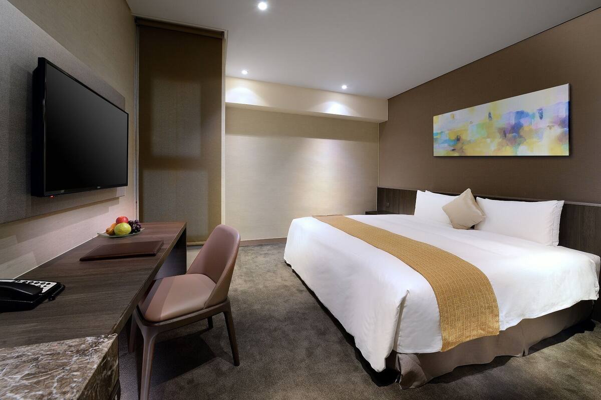 Ein Hotelzimmer mit Bett, Schreibtisch mit Stuhl, Flachbildfernseher und einem Bild an der Wand.