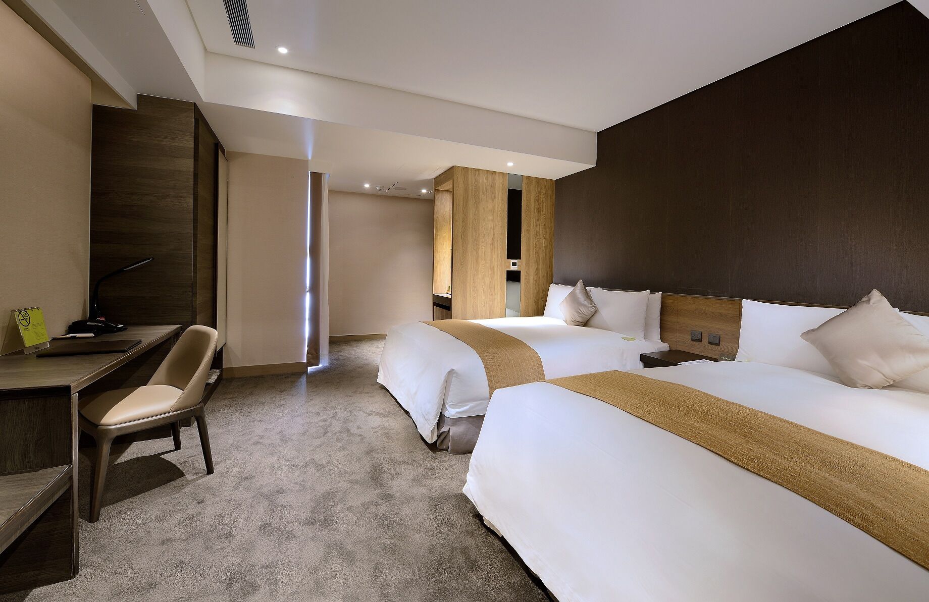 A hotel room with two beds, a desk, and a chair.