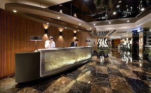 A modern hotel reception area with a marble reception desk, wooden panel walls, and a glass partition. - Hualien Holiday Hotel (Hualien City)