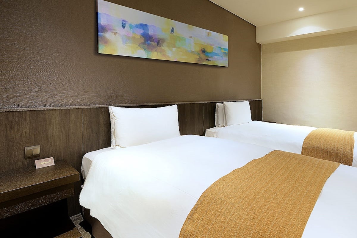 Ein Hotelzimmer mit zwei Betten, einem großen abstrakten Gemälde an der Wand und einem hölzernen Kopfteil.