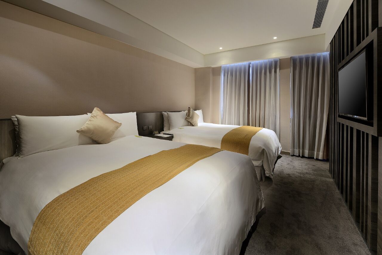 A hotel room with two beds, a TV, and a large window with curtains.