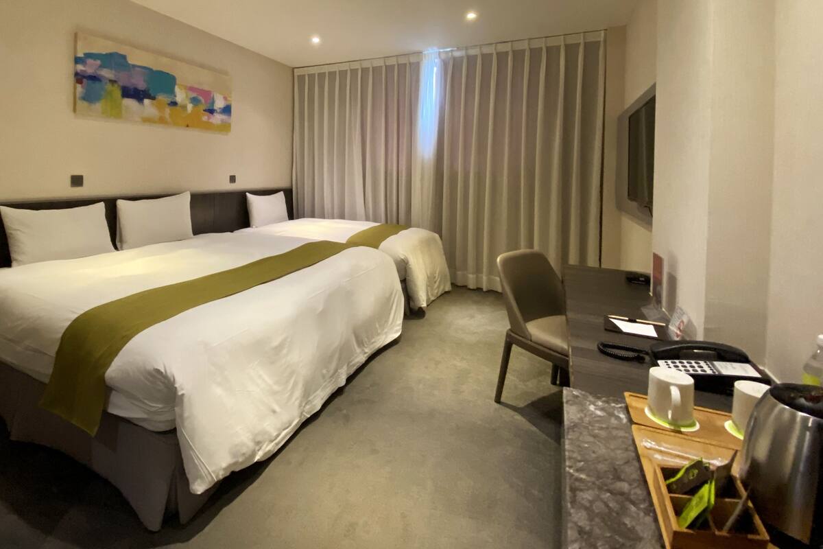 Ein Hotelzimmer mit zwei Betten, einem Schreibtisch mit Telefon und einem an der Wand befestigten Fernseher.