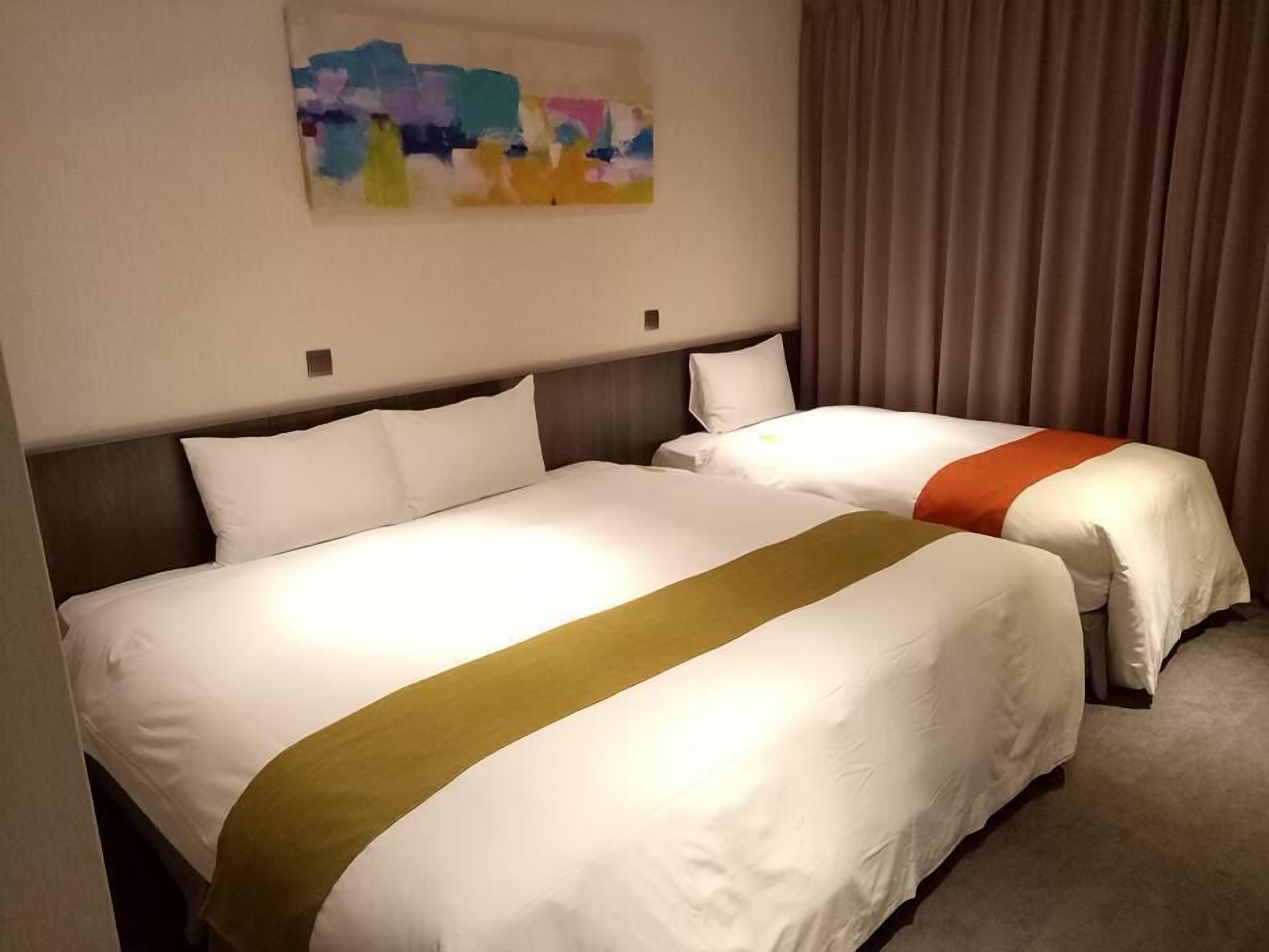 Una habitación de hotel con dos camas, un cuadro en la pared y una cortina.