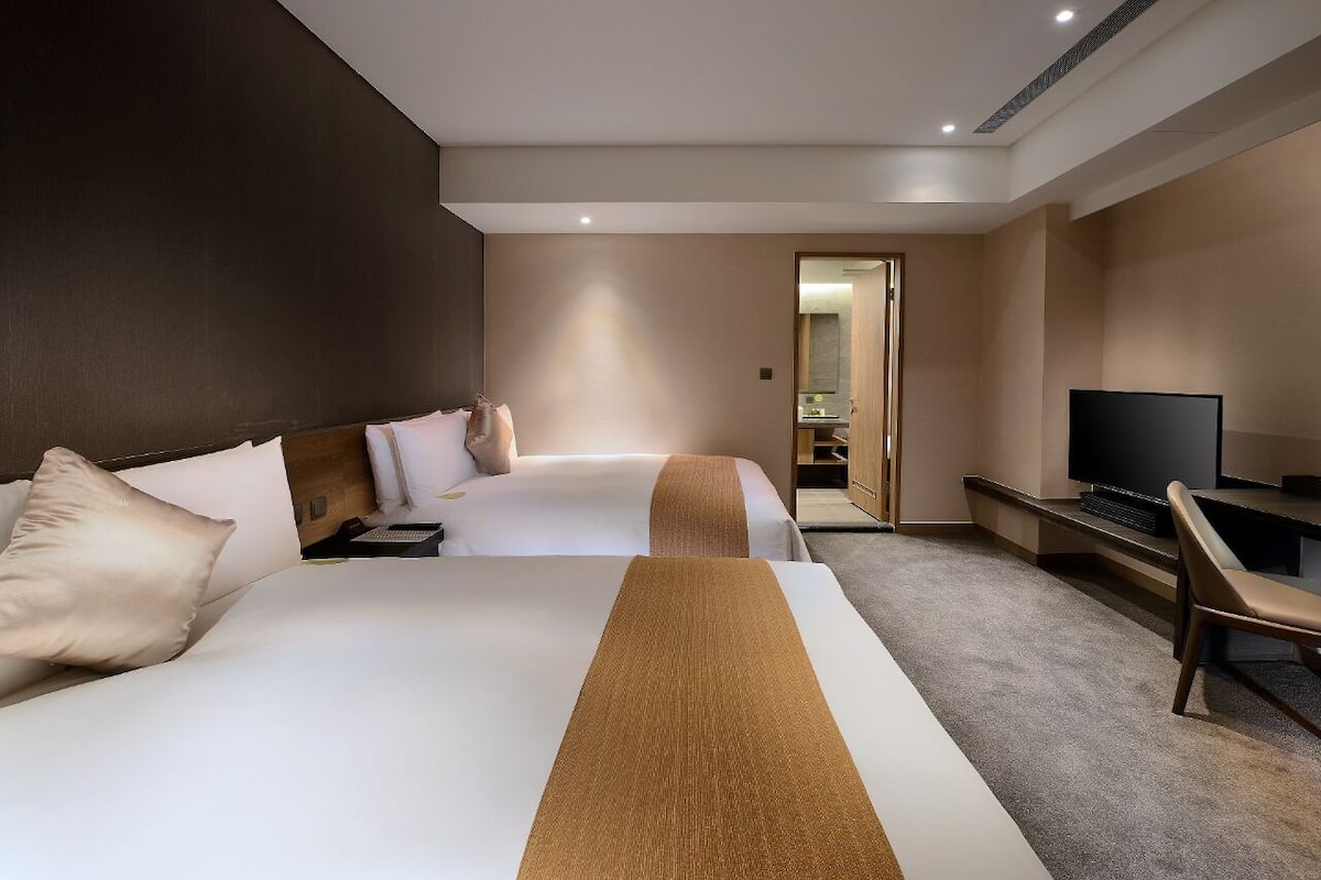 Ein Hotelzimmer mit zwei Betten, einem Fernseher, einem Schreibtisch und einem Spiegel.
