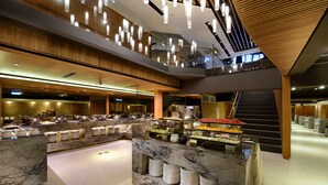 Un hall d’hôtel à plusieurs niveaux, doté d’un comptoir de réception en marbre, d’un espace buffet et d’un escalier menant à un étage supérieur.