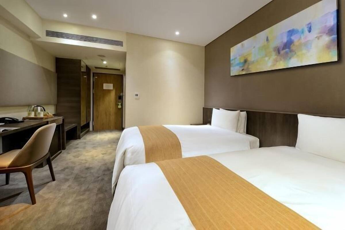 Ein Hotelzimmer mit zwei Betten, einem Schreibtisch, einem Stuhl und einem Bild an der Wand.