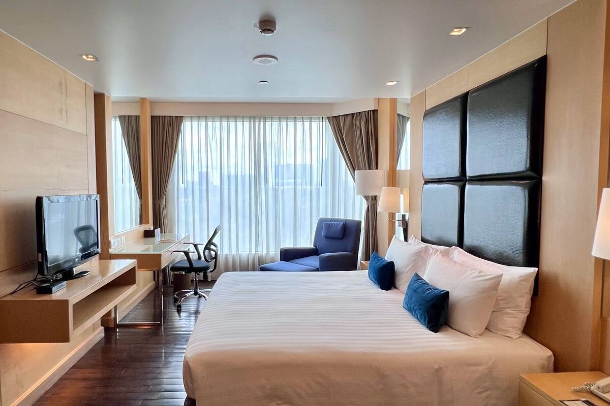 Una habitación de hotel con una cama grande, un escritorio, una silla, un televisor y una ventana con cortinas.