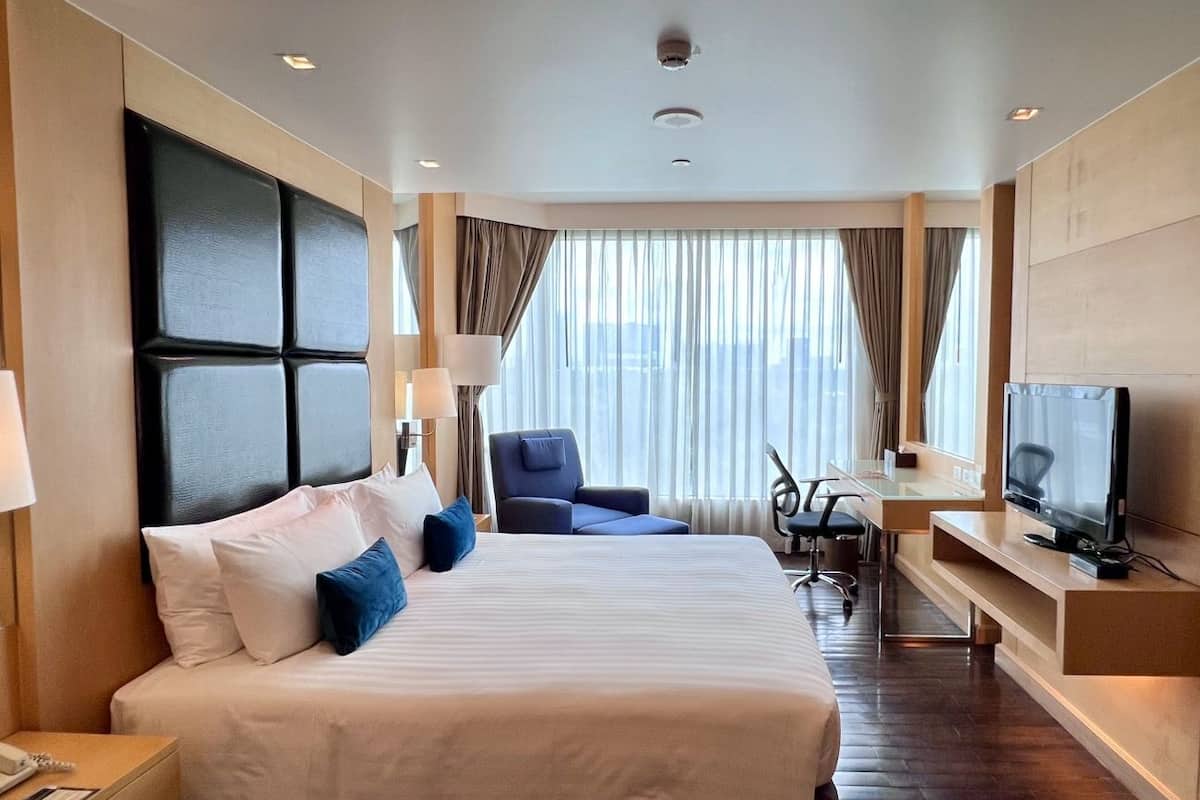 Habitación de hotel con una cama grande, un escritorio con silla, televisor y ventana con cortinas.
