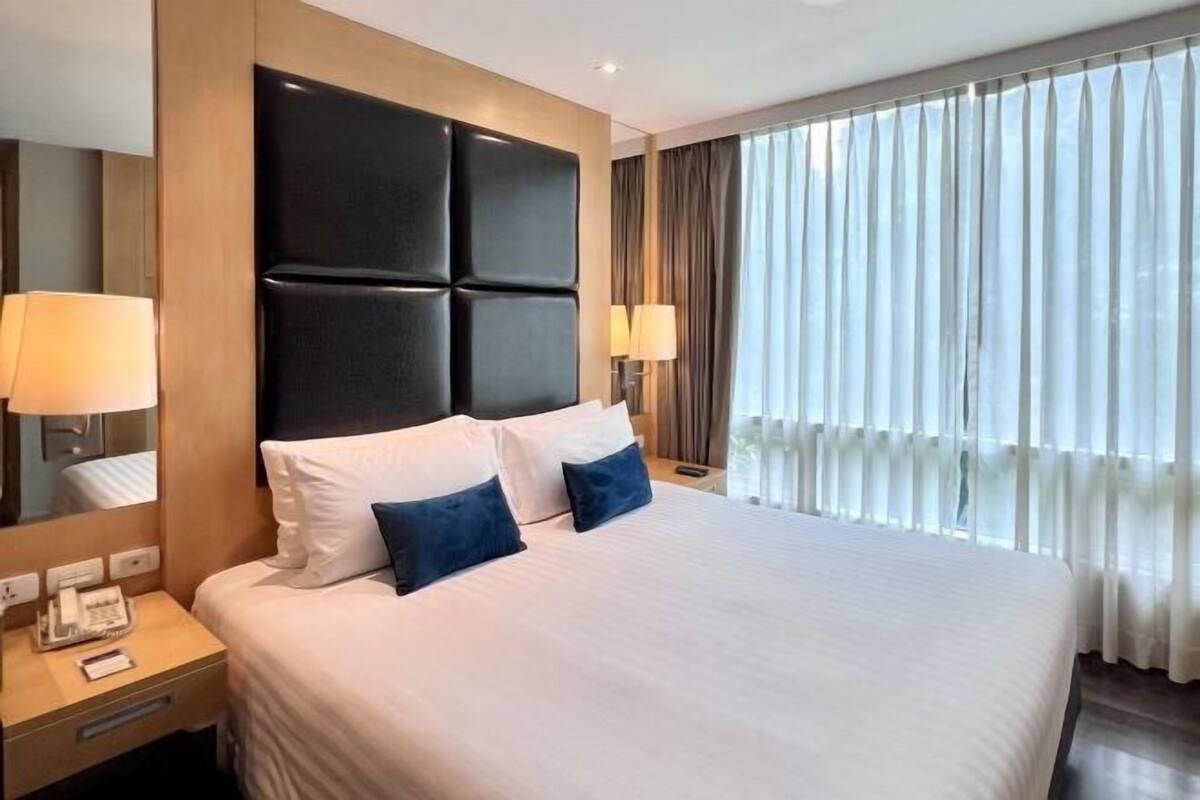 Habitación de hotel con una cama grande, cabecera, lámparas de noche, mesitas de noche y una ventana con cortinas.