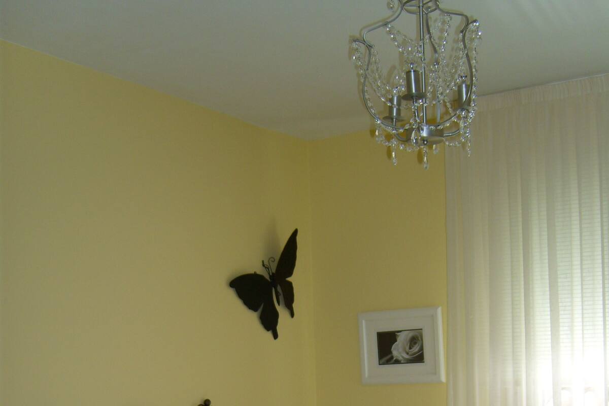 Un dormitorio con una cama, una araña, un adorno de mariposa en la pared y un cuadro enmarcado.