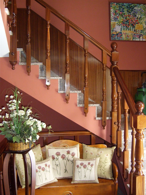 Una escalera con barandillas de madera, una cesta de mimbre con flores y un sofá con cojines estampados.