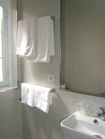 Un baño con un lavabo blanco, dos toallas blancas colgadas en ganchos, un espejo y una ventana.