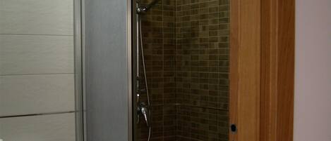 Un baño con cabina de ducha, inodoro y pared con azulejos.
