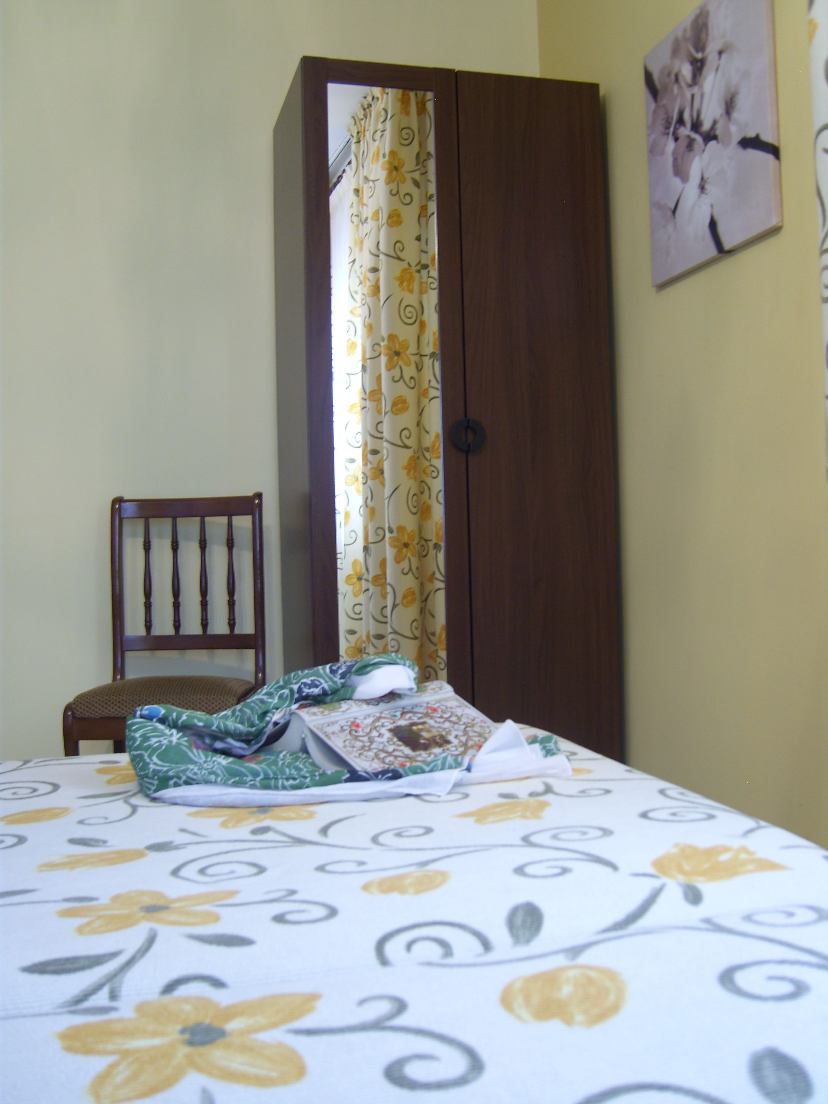 Ein Schlafzimmer mit einem Bett, einem Holzschrank, einem Stuhl und einem Vorhang mit Blumenmuster.