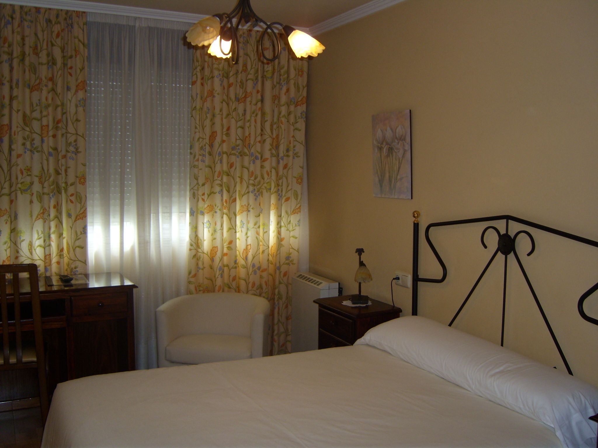 Een slaapkamer met een bed, een bureau, een stoel, een nachtkastje en een lamp.