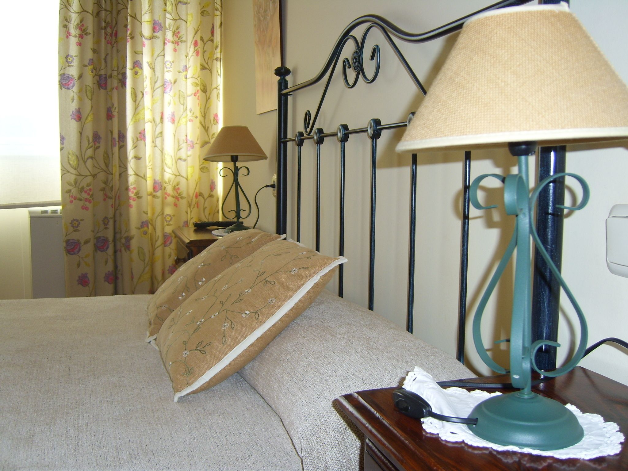 Een opgemaakt bed met een sierkussen met bloemenprint en een lamp op een nachtkastje.