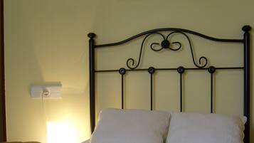 Een bed met witte kussens en een zwart metalen hoofdbord. Boven het bed hangt een foto in een lijst aan een witte muur.