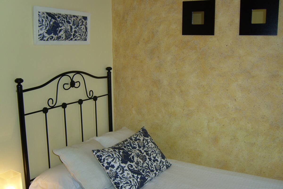 Una cama con cabecera de metal, ropa de cama blanca y una almohada estampada.