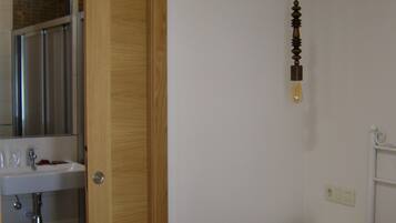Un dormitori amb un llit, una taula de nit, una porta de fusta i un bany amb un lavabo i un mirall.