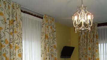 Habitación de hotel con cortinas florales, una cama con colcha estampada, un candelabro y un televisor en la pared.